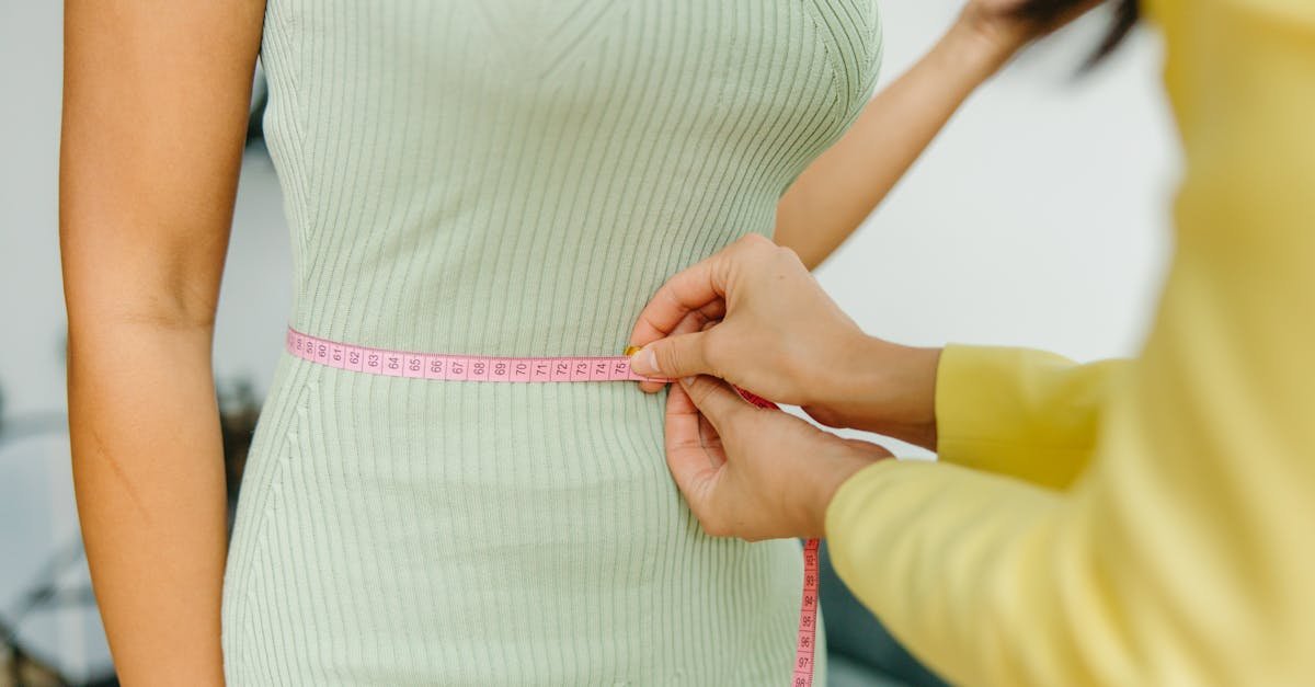 A tailor carefully measures a woman's waist with a pink tape measure, highlighting elegance and fit.